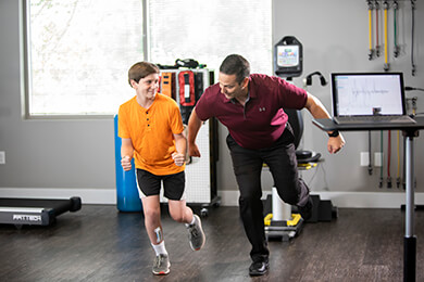 Male therapist doing one-leg balance exercises with a young therapy patient.
