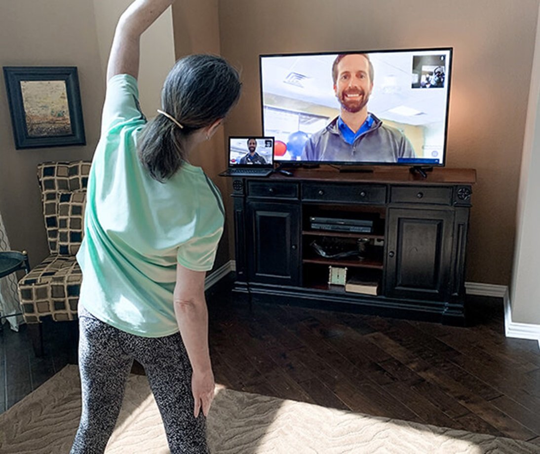 Woman exercising in her living room using a television to get instruction from a physical therapist.