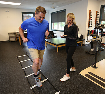 A man is running through an agility ladder drill while a therapist is beside with a stopwatch