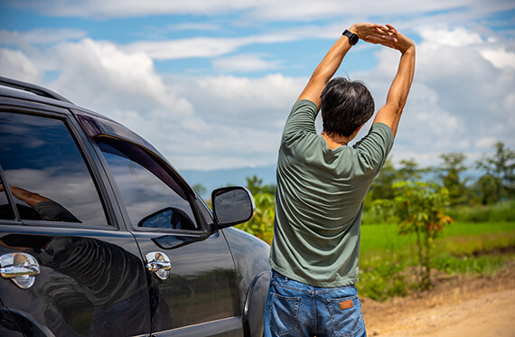 Man standing beside his car and facing away from camera. He is holding his hands above his head to stretch his upper body