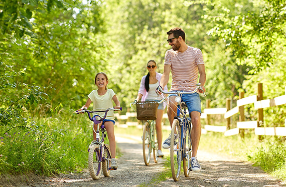 Dad, mother and daughter smiling and riding bikes together outdoors